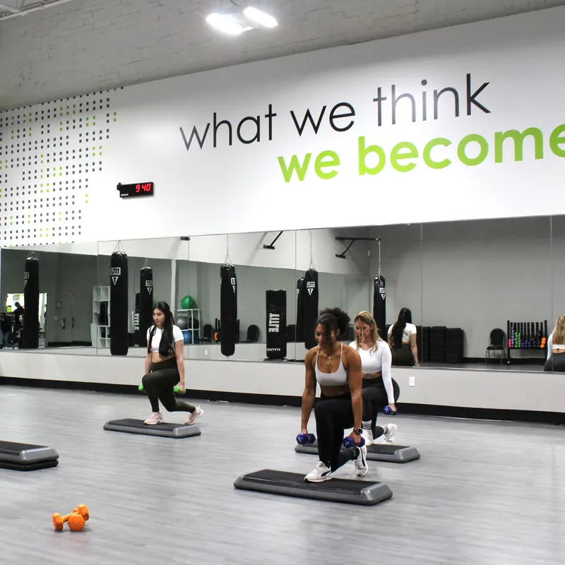 Three women in the studio lunging onto steps with dumbbells in their hands.